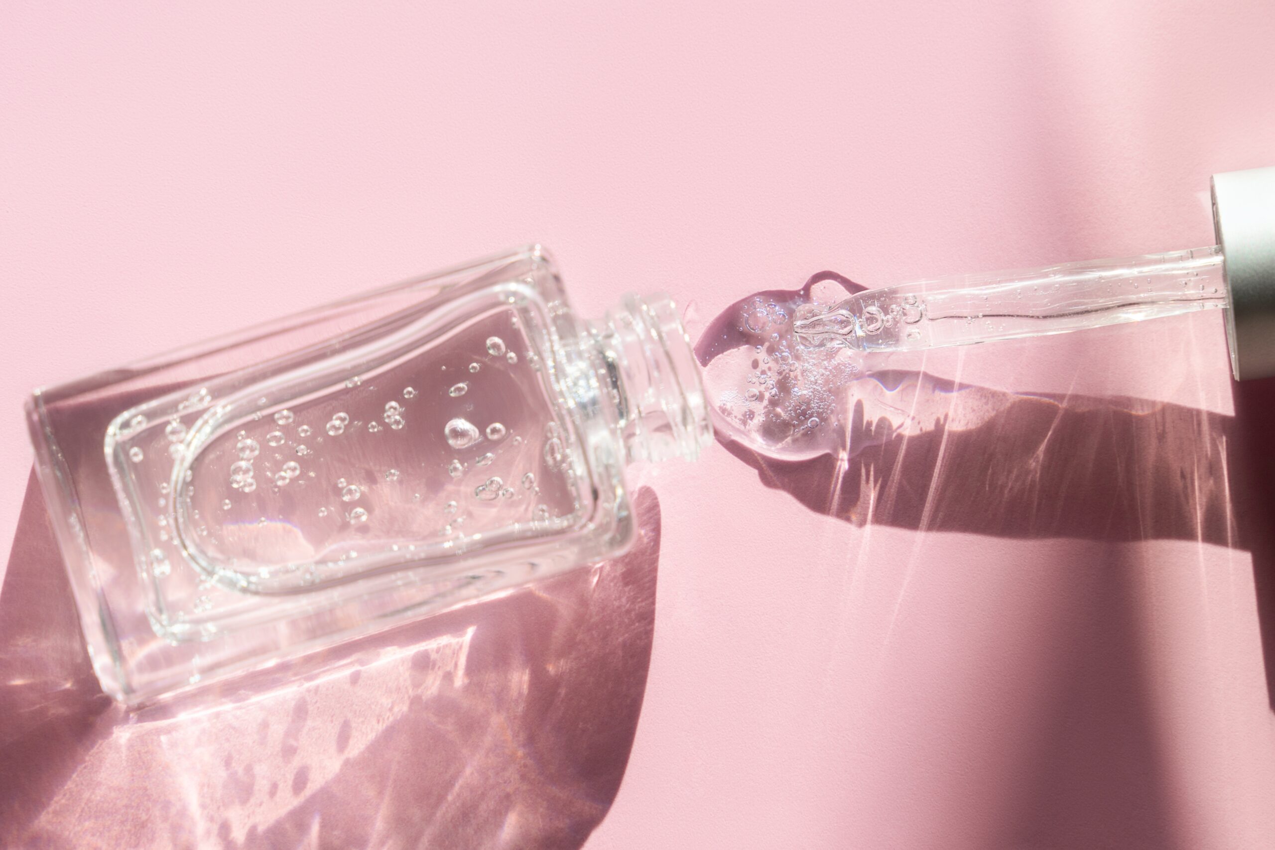 Glass bottle with hyaluronic acid, hydration skin with shadows on pastel pink background.